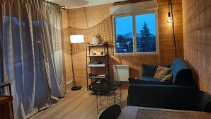 Un interior acogedor de cabaña con detalles de madera, un comedor, un sofá y una ventana con vistas a árboles y montañas.