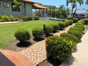 A landscaped garden with a paved walkway, trimmed hedges, and a building with a tiled roof.
