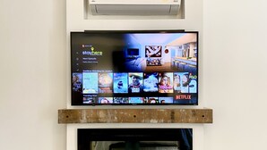 A modern living room with a flat-screen TV mounted above a fireplace, a surfboard, and a couch. - Escape WithInn-Relaxation Centrally Located to Beaches and Walkable Restaurants (Harbert)