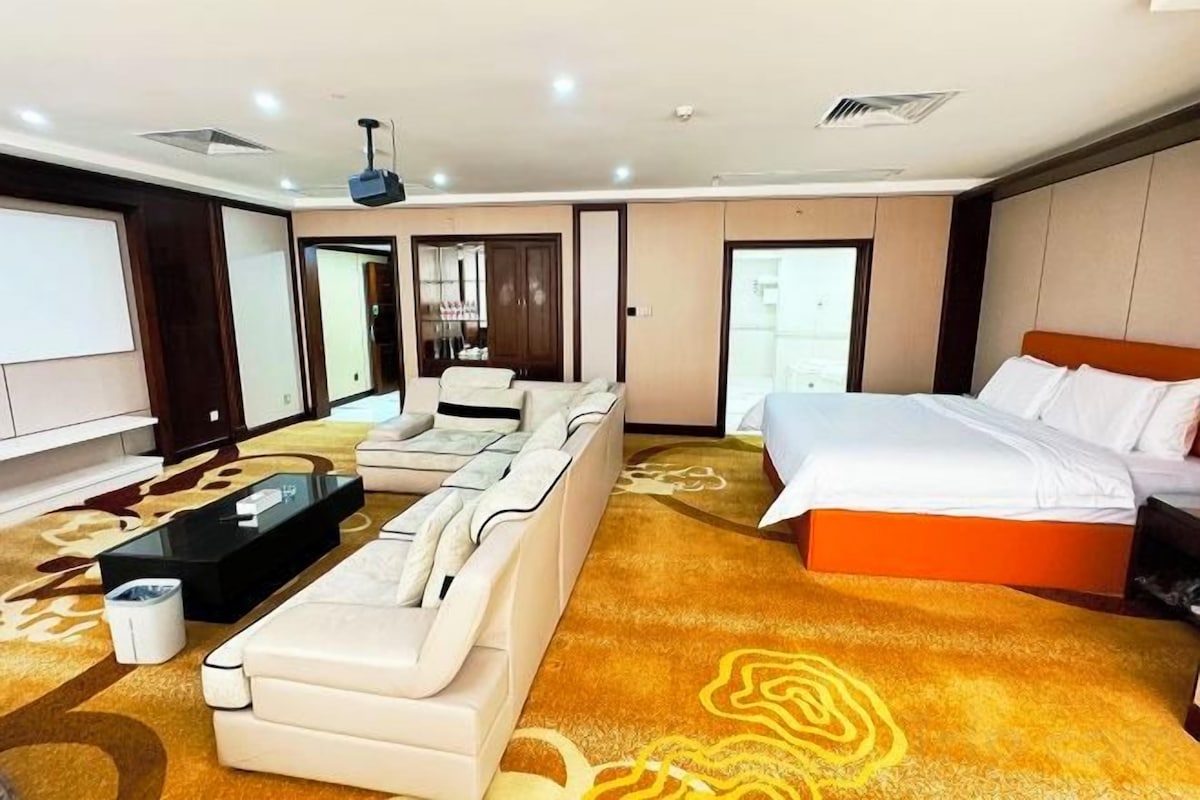 A hotel room with a large bed, a sofa, a coffee table, and a television.