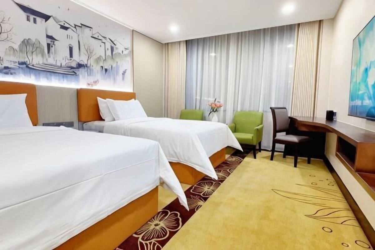 A hotel room with two beds, a desk, a chair, and a TV.
