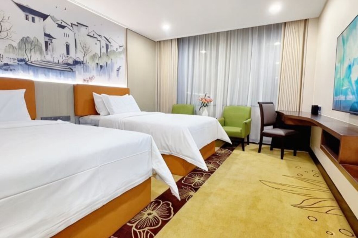 A hotel room with two beds, a desk, a chair, and a TV.