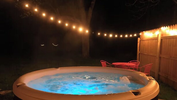 Ett bubbelbad med ett trästaket och ljusslingor i bakgrunden.