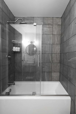 Un baño moderno con ducha envuelta en vidrio, bañera y tocador con espejo.
