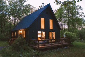 A dark wooden cabin with a steep roof, large windows, and a wooden deck. - Stony Kill Cabin: A-Frame Kerhonkson Getaway with Modern Kitchen & Firepit (Kerhonkson)