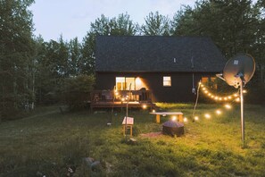 Una casa con terraza, antena parabólica y luces colgantes en el jardín.