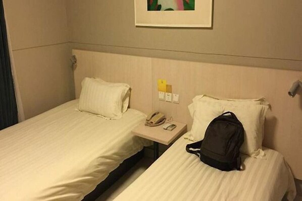 Une chambre d’hôtel avec deux lits, une table de chevet avec un téléphone et une lampe, et un tableau encadré au mur.