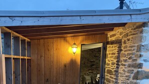 An outdoor patio area with wooden flooring, a stone wall, and a seating arrangement including a sofa and two chairs. - Longere LE Penty - Plougonvelin (Plougonvelin)