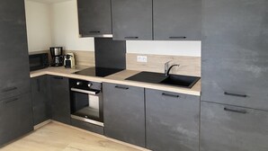 A modern kitchen with dark cabinets, a black countertop, a built-in oven, and a sink. - Longere LE Penty - Plougonvelin (Plougonvelin)