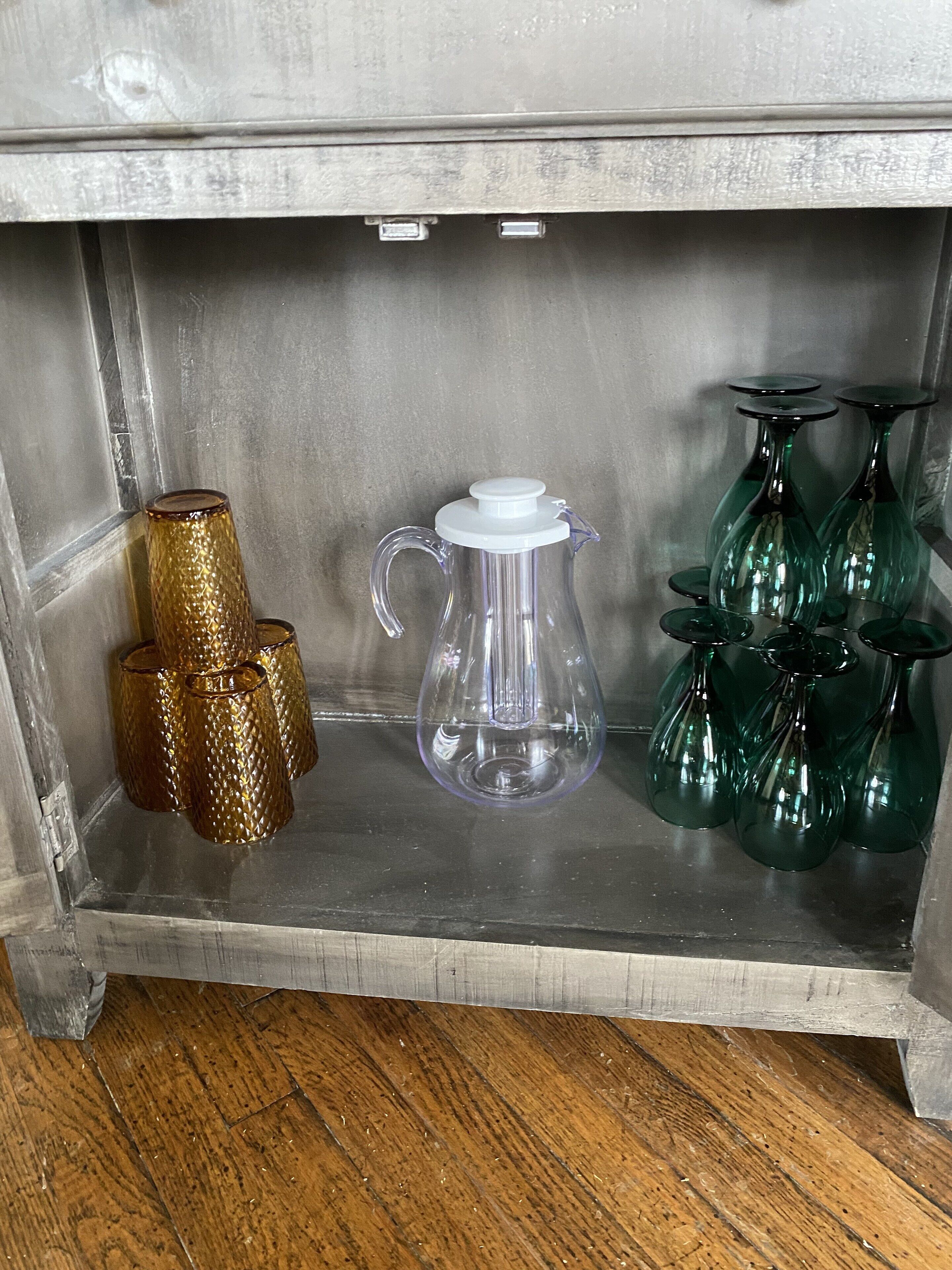 Una estantería con una cafetera, tres vasos de vidrio y un juego de jarrones de vidrio verde.