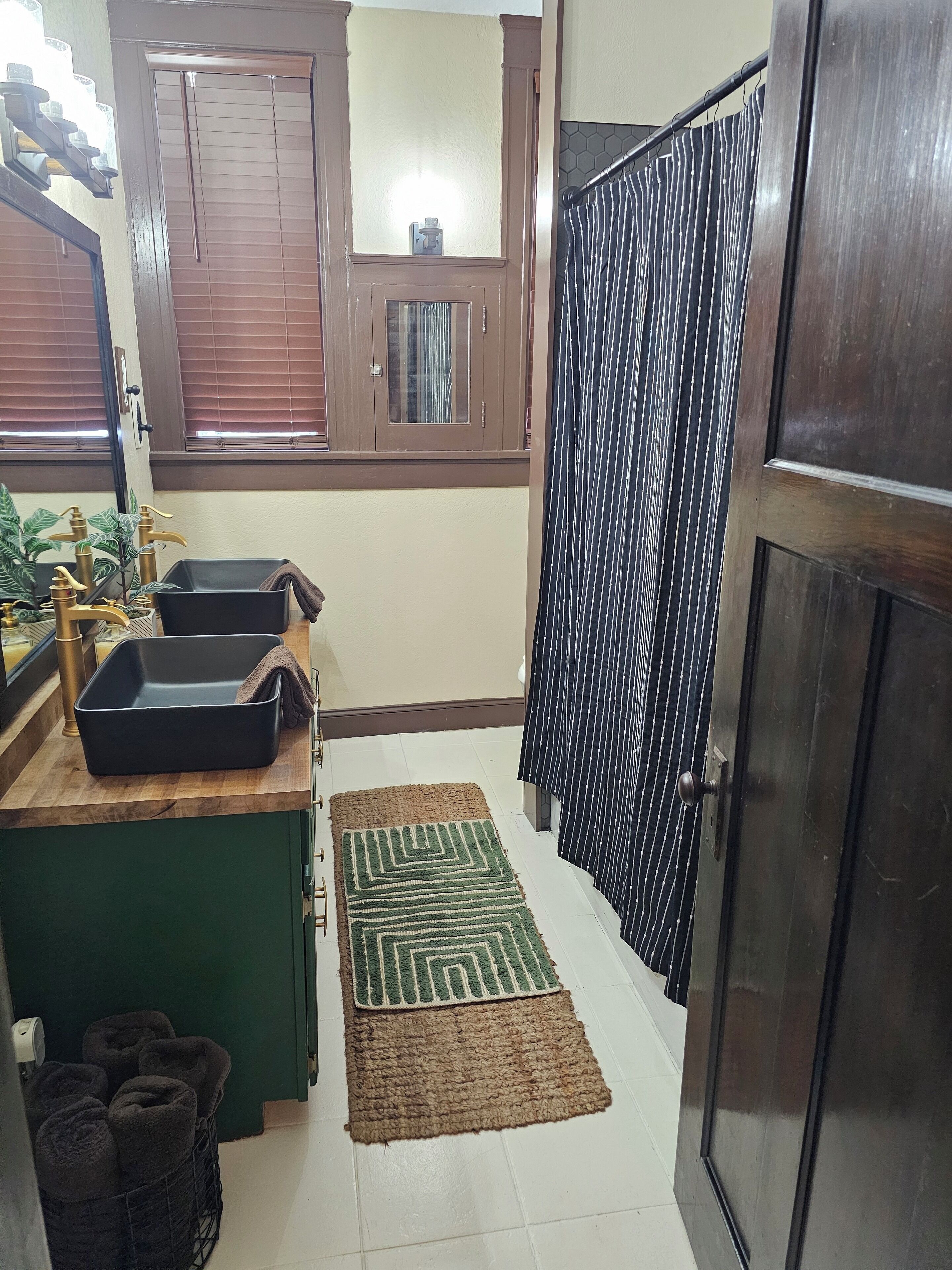 A small kitchen with a sink, a window with blinds, a mirror, and a door with a striped curtain.