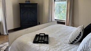 Un dormitorio con cama, ventilador de techo, ventana con cortinas, cómoda y mesita de noche.