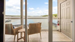 Een balkon met twee rieten stoelen en een klein tafeltje, met uitzicht op een waterpartij en een verre kustlijn.