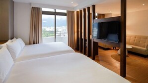 Habitació d'hotel amb dos llits, una televisió, un sofà i una finestra gran amb cortines.