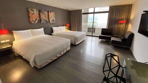 Habitació d'hotel amb dos llits, un sofà, una televisió i obres d'art a la paret.