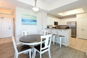 A modern kitchen with white cabinets, a stainless steel refrigerator, a microwave, and a dining area with a round table and white chairs. - 1st Floor condo at The Palms of Destin with Free Beach Shuttle! (Destin)