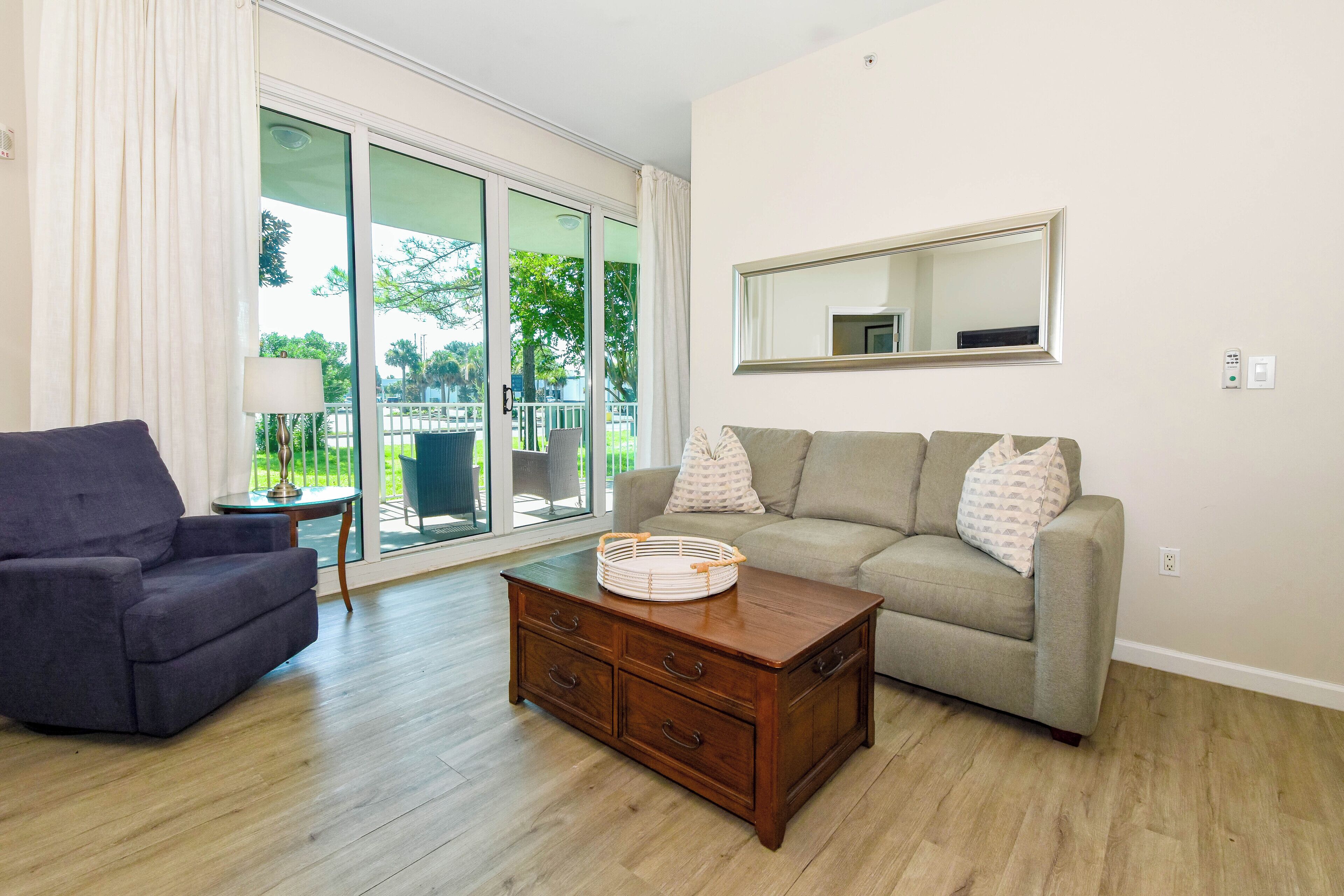 A living room with a sofa, a chair, a coffee table, and a sliding glass door leading to an outdoor area.