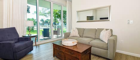 A living room with a sofa, a chair, a coffee table, and a sliding glass door leading to an outdoor area.