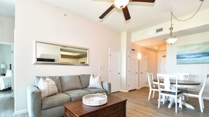 A living room with a gray sofa, a wooden coffee table, and a dining area with white chairs and a table. - 1st Floor condo at The Palms of Destin with Free Beach Shuttle! (Destin)