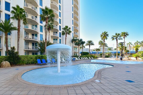 A hotel pool area with a water feature, lounge chairs, and palm trees.
