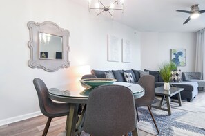 A modern living room with a dining area, featuring a round table, chairs, a sofa, and a ceiling fan.