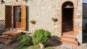 A stone building with a wooden door, a small staircase, and potted plants. - Farmhouse in the greenery of the Tuscany countryside with private pool and view (Murlo)
