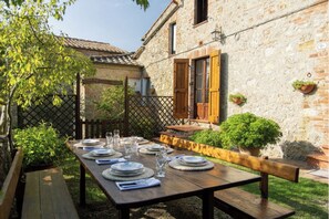 Une table en bois, installée à l’extérieur, avec des assiettes, des verres et un banc.
