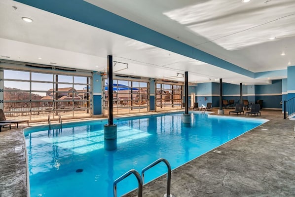 En indendørs swimmingpool med glasvægge, udsigt til det fri og en betongulv.