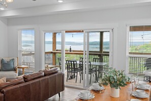 A spacious living area with a sliding glass door leading to an outdoor deck with a table and chairs. - High-End Modern Retreat-Peaceful Water Views-Pvt Hot Tub-Dog-Friendly-Cmty Pools-Free Tickets (Branson)
