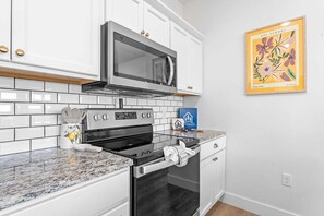 A kitchen with white cabinets, a stainless steel microwave, a stove, and a tiled backsplash.