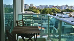 A balcony with a table and chairs, offering a view of a cityscape with buildings and trees. - A Estrenar con Piscina y gym en el Centro!! (Santo Domingo)