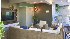 A modern living area with a flat-screen TV, wicker sofa, and a bar area with stools. - A Estrenar con Piscina y gym en el Centro!! (Santo Domingo)