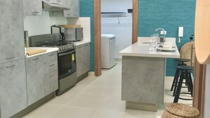 A modern kitchen with grey cabinets, a stove, and a dining area with a table and chairs. - A Estrenar con Piscina y gym en el Centro!! (Santo Domingo)