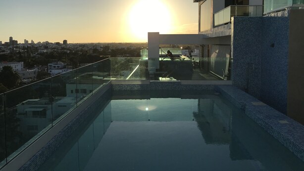 A rooftop pool with a glass balustrade, a clear view of the sunset, and a cityscape in the background. - A Estrenar con Piscina y gym en el Centro!! (Santo Domingo)