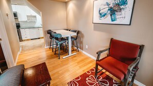 A dining area with a table and chairs, a red upholstered chair, and a painting on the wall.