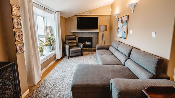 A living room with a sectional sofa, a fireplace, a flat-screen TV, and a window with curtains.