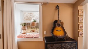 A room with a large window, a guitar, a cabinet with intricate carvings, and framed pictures on the wall.