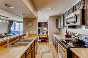A modern kitchen with stainless steel appliances, wooden countertops, and a visible clock on the wall.