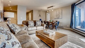 A living room with a sectional sofa, a wooden coffee table, and a dining area with chairs and a table. - Lake Dillon! Ampitheatre, Walk to Lake,Pool&HT (Dillon)