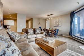A living room with a sectional sofa, a wooden coffee table, and a dining area with chairs and a table. - Lake Dillon! Ampitheatre, Walk to Lake,Pool&HT (Dillon)