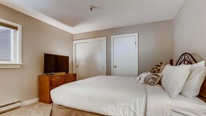 A bedroom with a large bed, a television on a wooden dresser, and two doors. - Lake Dillon! Ampitheatre, Walk to Lake,Pool&HT (Dillon)