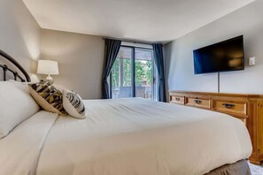 A hotel room with a large bed, a TV mounted on the wall, a wooden dresser, and a balcony with curtains. - Lake Dillon! Ampitheatre, Walk to Lake,Pool&HT (Dillon)
