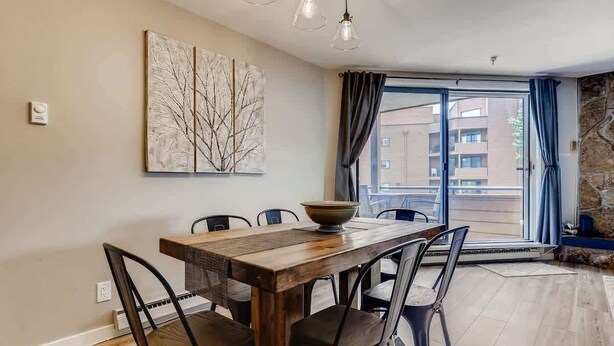 A dining area with a wooden table and chairs, a large abstract painting, and a view through a glass door. - Lake Dillon! Ampitheatre, Walk to Lake,Pool&HT (Dillon)