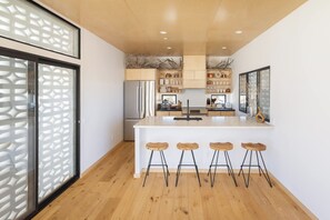 A modern kitchen with a central island, wooden stools, and built-in cabinetry. - Neutra Home Joshua Tree Luxury Retreat Pool and Spa (Joshua Tree)