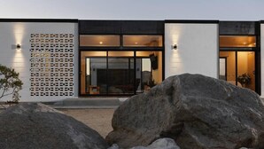Un bâtiment moderne doté de grandes fenêtres, d’un mur décoratif et d’un jardin de rocaille au premier plan.