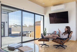 A modern living room with a large sliding glass door leading to an outdoor area, a flat-screen TV mounted on the wall, and a comfortable seating area with a coffee table.