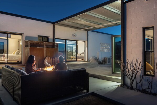 An outdoor seating area with a fire feature, a covered patio, and a view of the interior of a building. - Neutra Home Joshua Tree Luxury Retreat Pool and Spa (Joshua Tree)