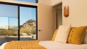 Une chambre avec un grand lit, une vue sur un paysage rocheux par une porte vitrée et un luminaire fixé au mur.