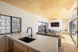 A modern kitchen with a large island, a built-in sink, and a dining area with a sofa and a TV.
