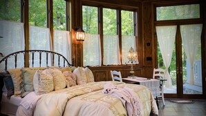 Un dormitorio con una cama grande, una mesita de noche, una mesa con una silla y una ventana con cortinas.